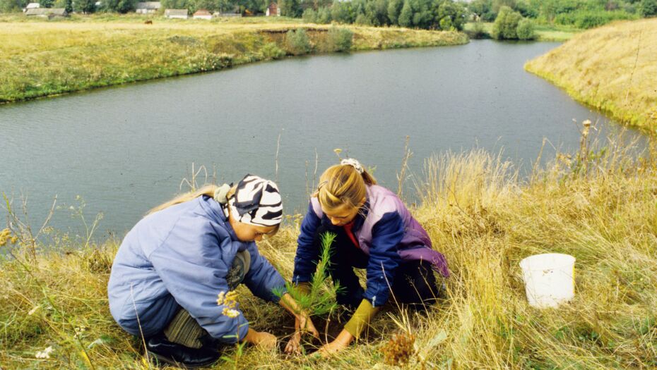 Zwei Mädchen pflanzen Setzlinge am Flussufer.