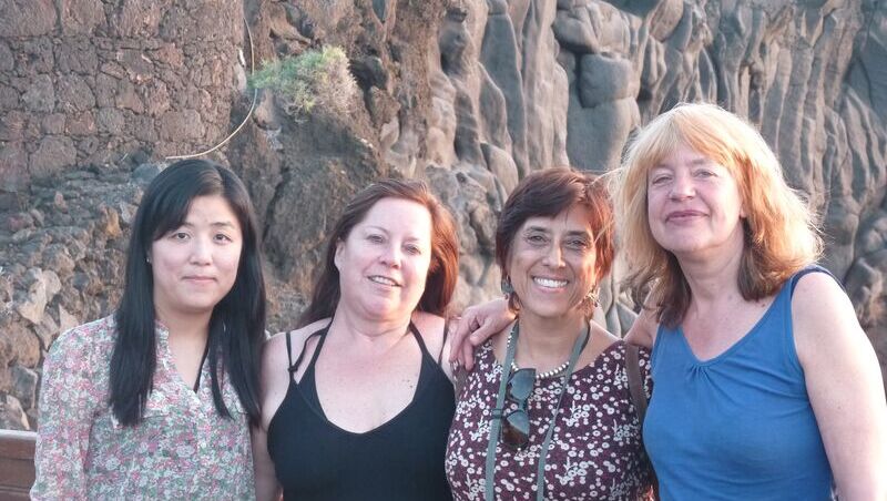 Vier Frauen stehen arm in arm von der Sonne bestrahlt vor einer Steinwand auf el Hierro.