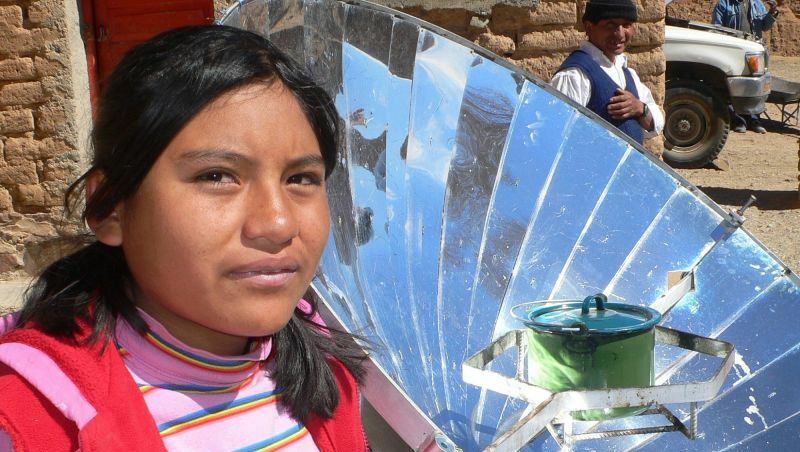 Ein Mädchen aus den Hochanden blickt in die Kamera, im Hintergrund ein großes, rundes Solarpanel.