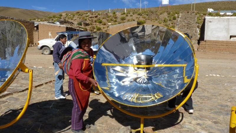 Eine Frau steht lächelnd neben einem großen, runden Solarpanel.