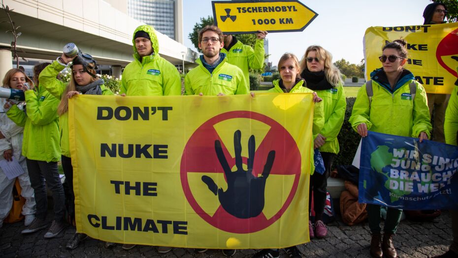 Eine Gruppe Demonstrierende mit einem großen, gelben Banner mit dem Schriftzug "don't nuke the climate" in schwarzen Großbuchstaben. Im Hintergrund sind Wolkenkratzer zu sehen.