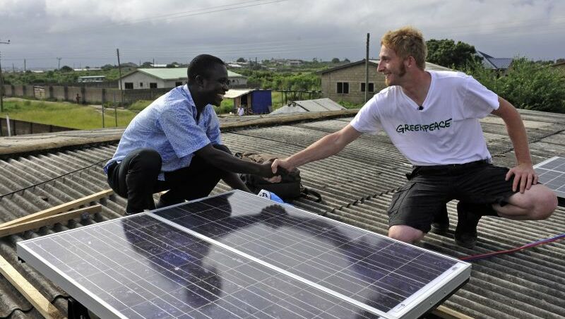 Zwei Männer, auf einem Dach neben einem Solar Panel, lachen und geben sich die Hand.
